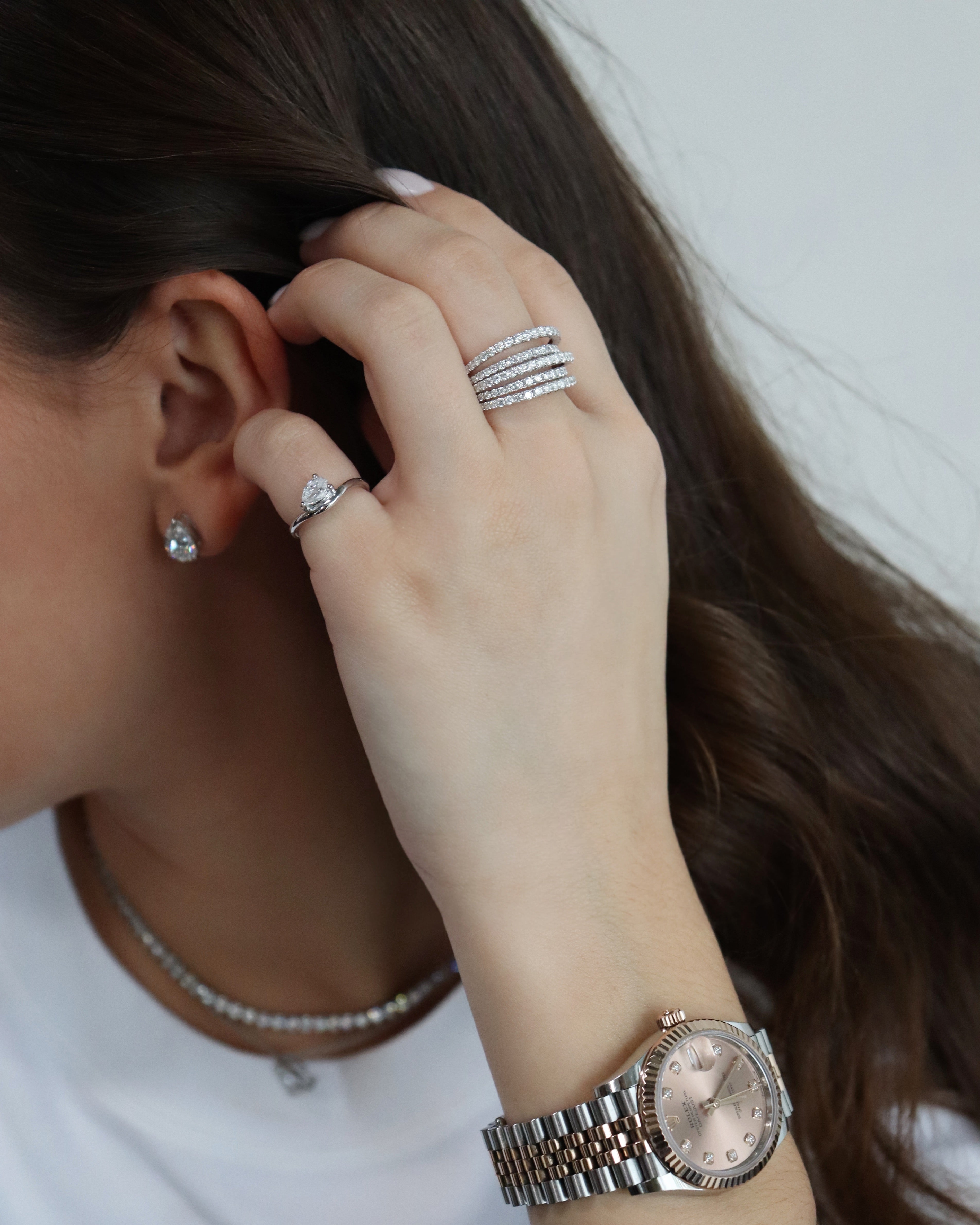 Close-up of a person's hand with jewelry, including rings and a watch, on a neutral background.