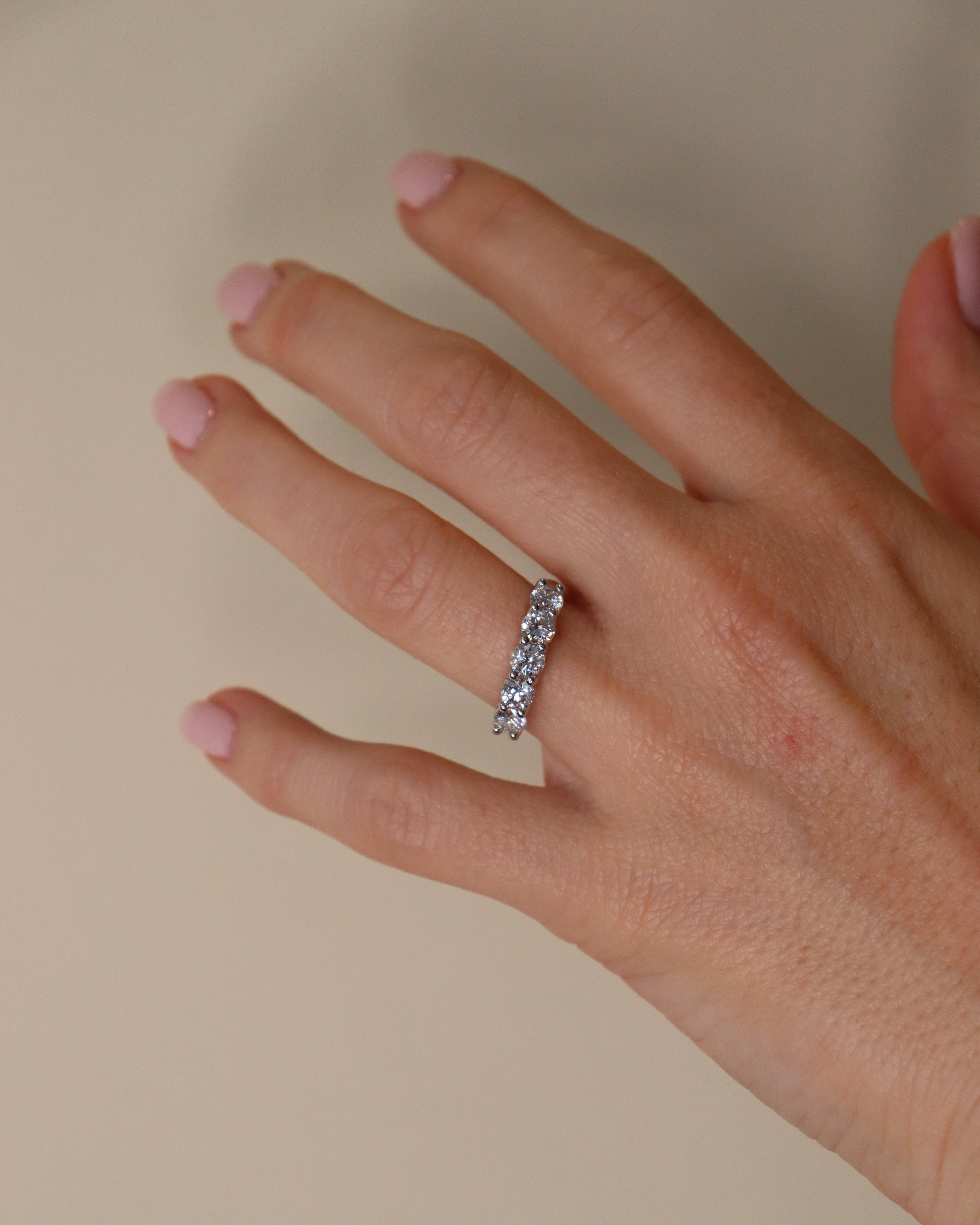 Hand wearing a silver ring with a clear stone on a beige background