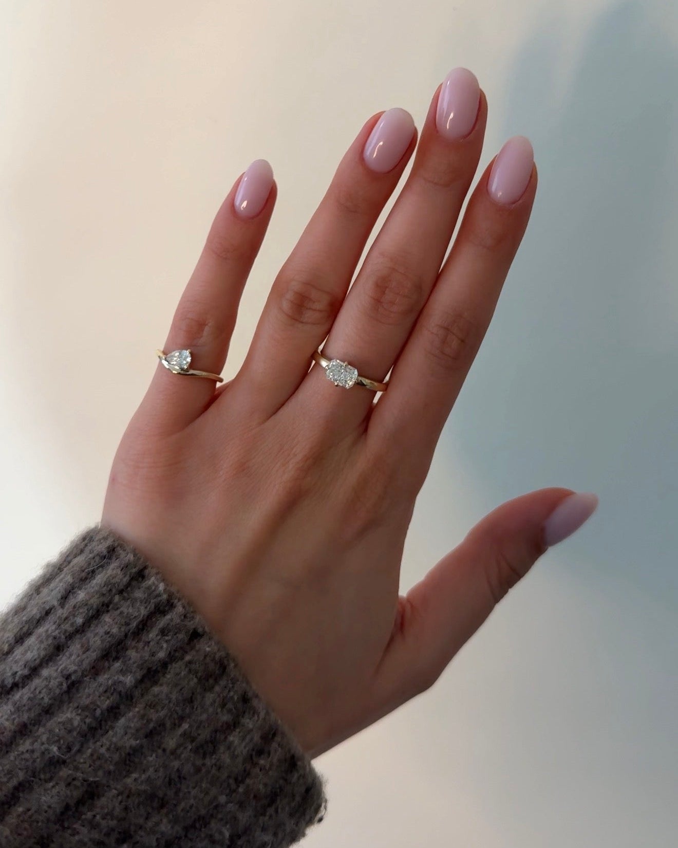 Hand wearing two diamond rings on a neutral background