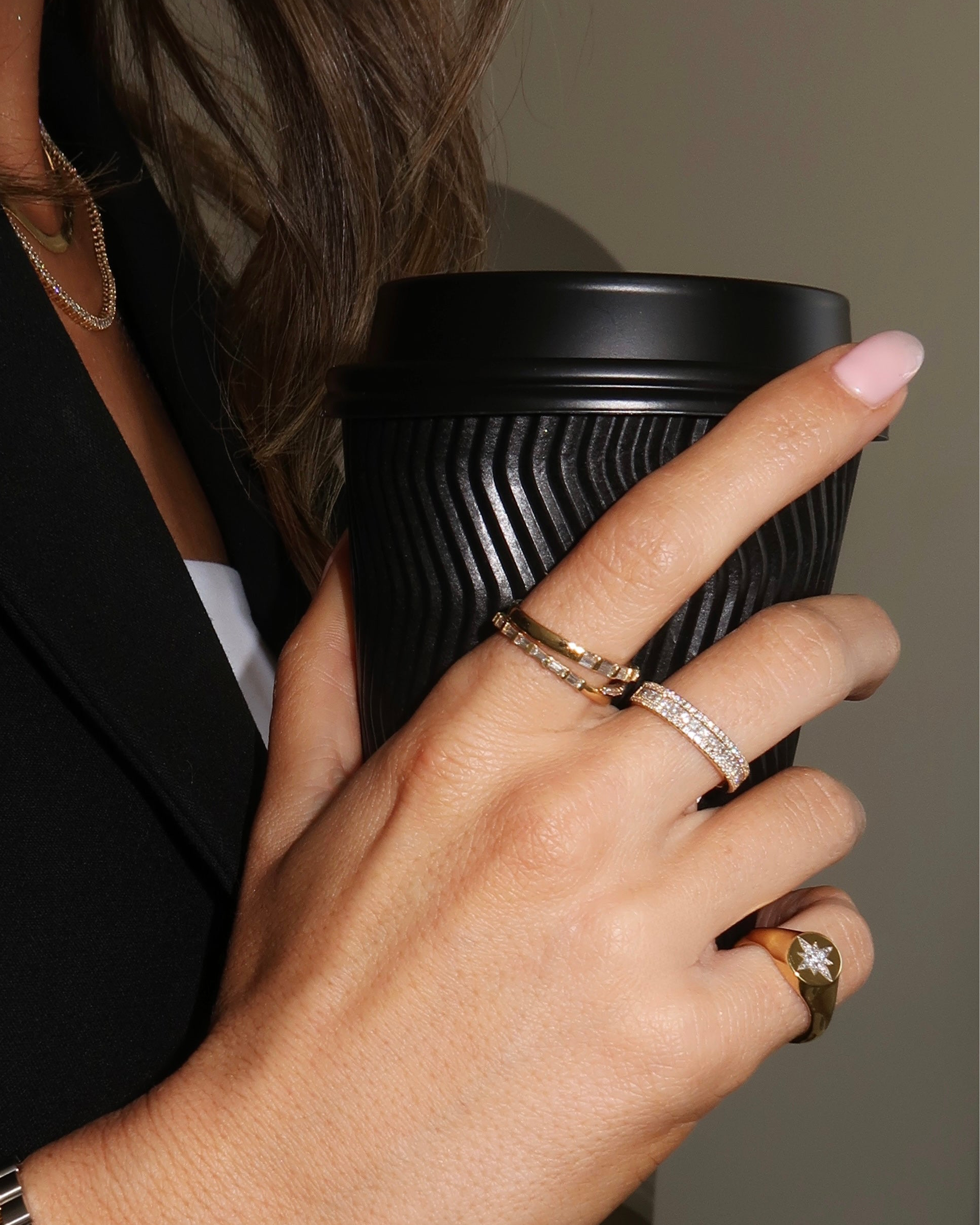 Hand holding a black coffee cup with jewelry on fingers