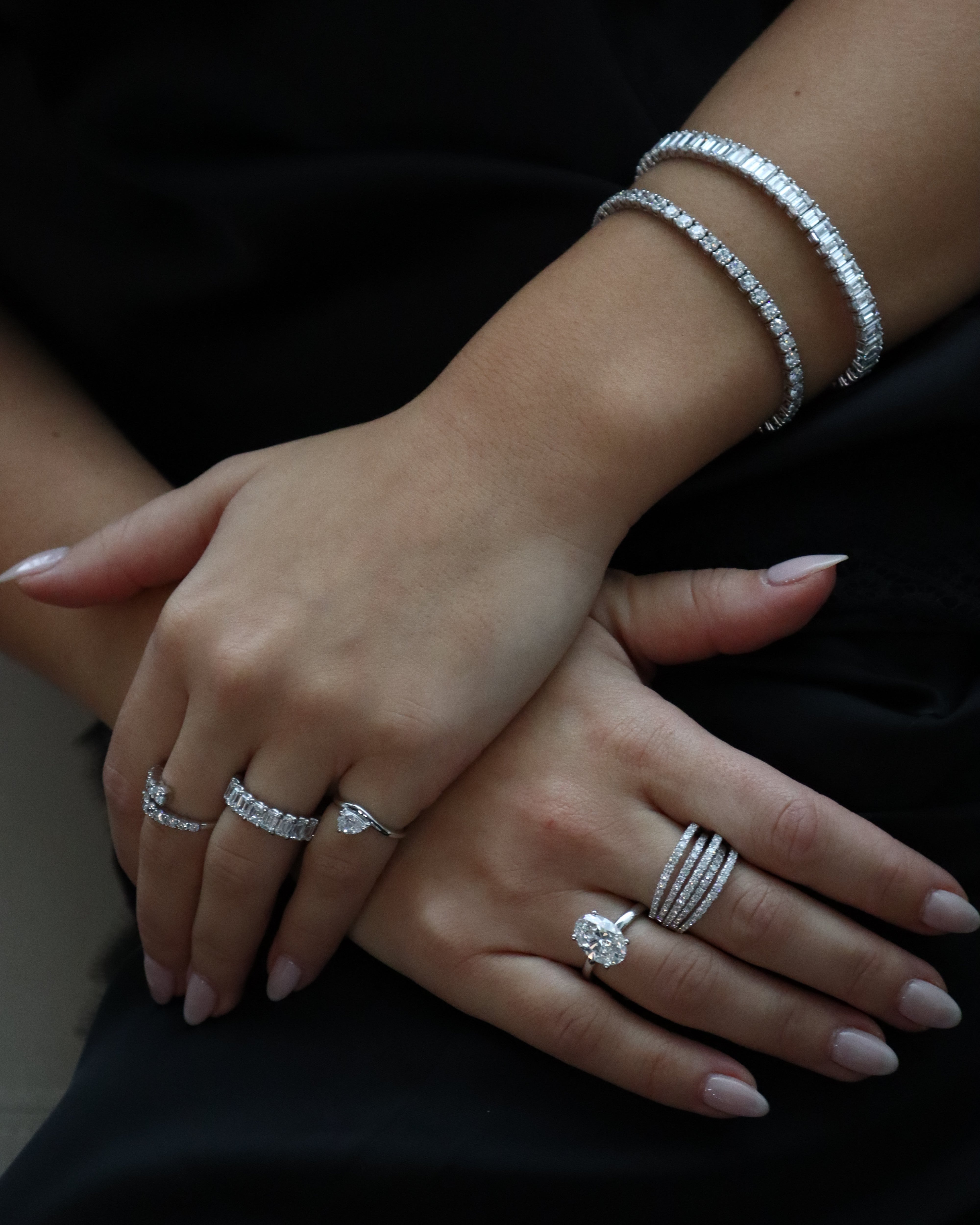Close-up of hands with multiple diamond rings and a bracelet on a dark background