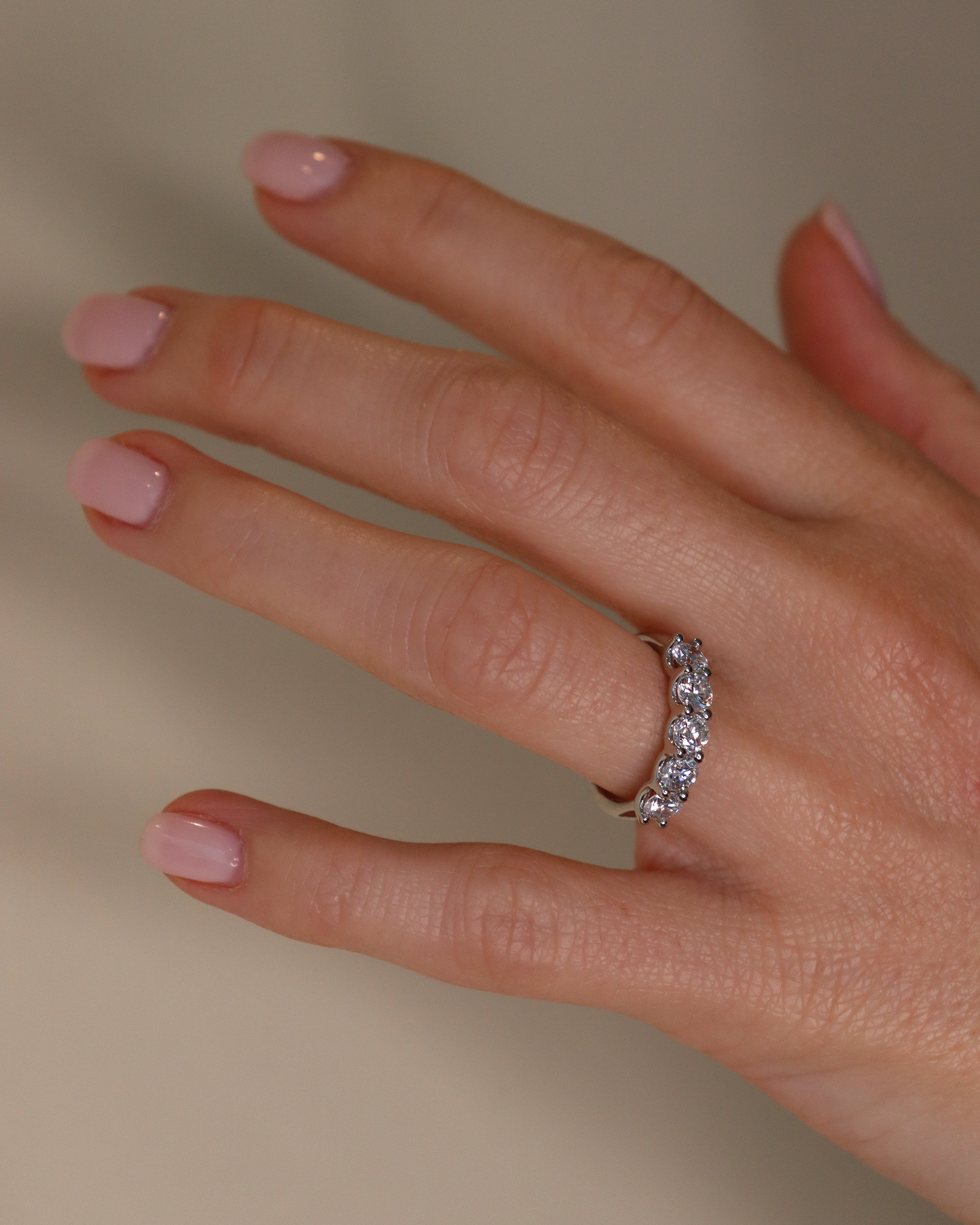 Hand wearing a diamond ring with pink nail polish on a neutral background