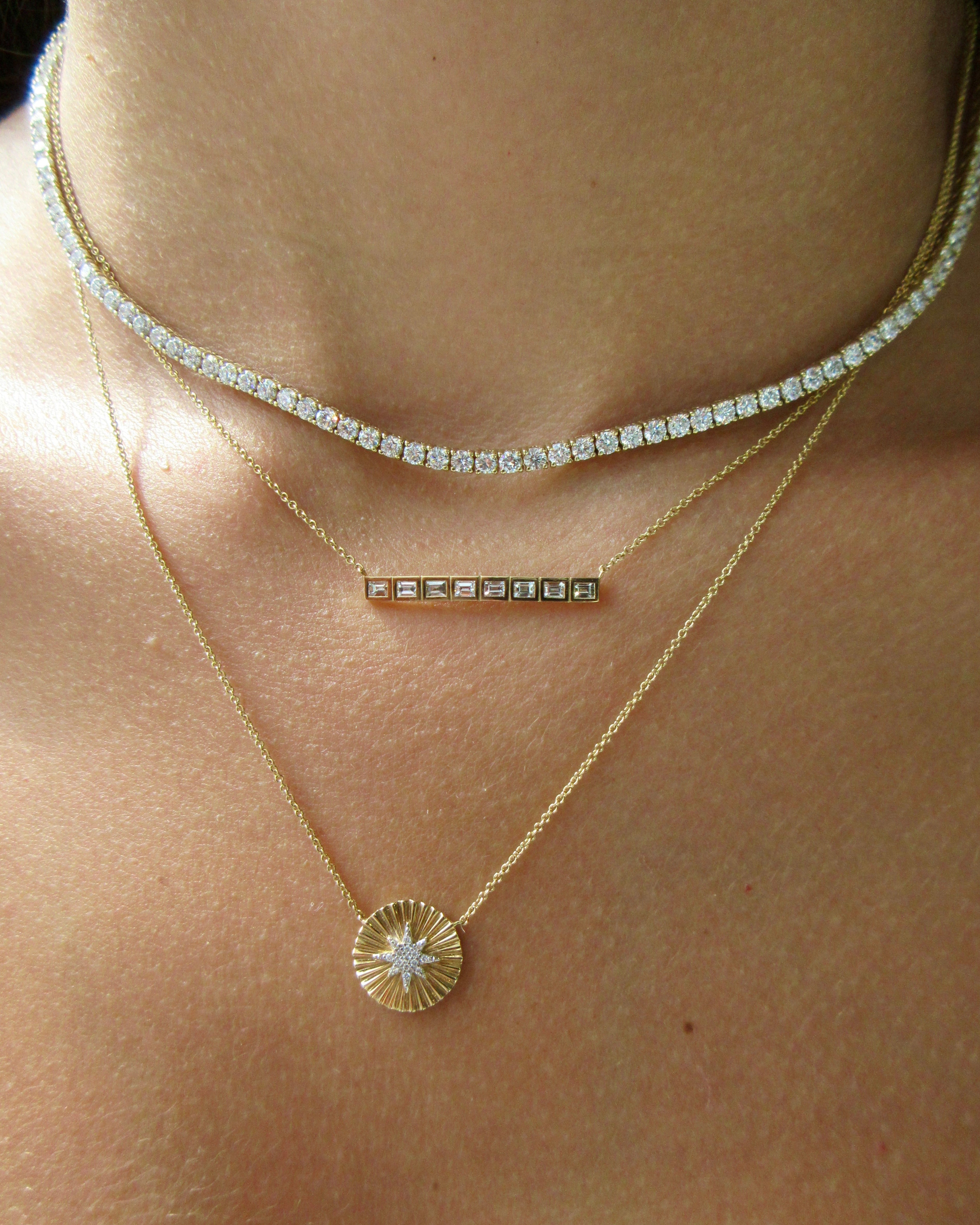 Close-up of a person wearing two gold necklaces with star designs on a light skin background.