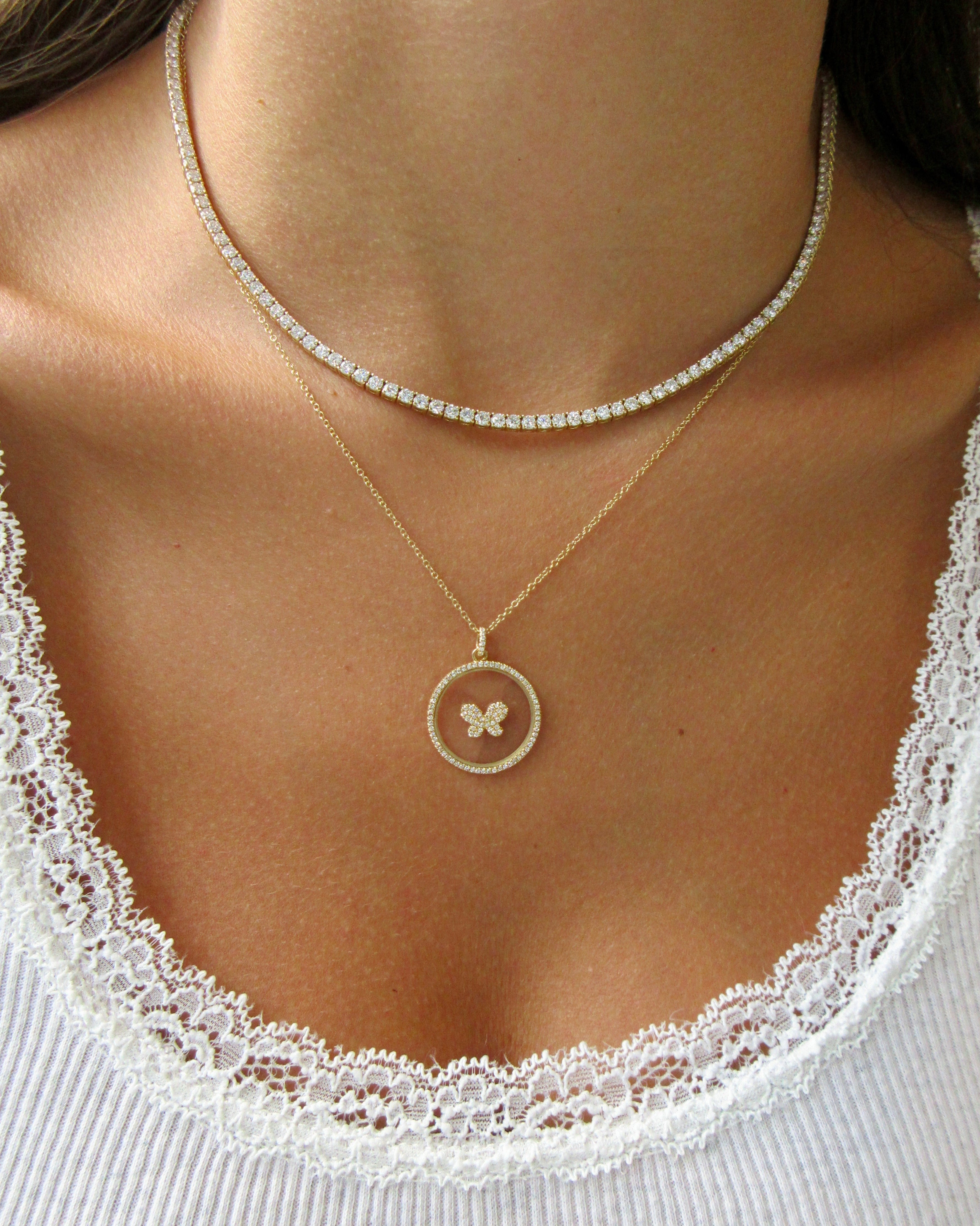 Close-up of a person wearing two necklaces with a butterfly pendant on a white lace top.