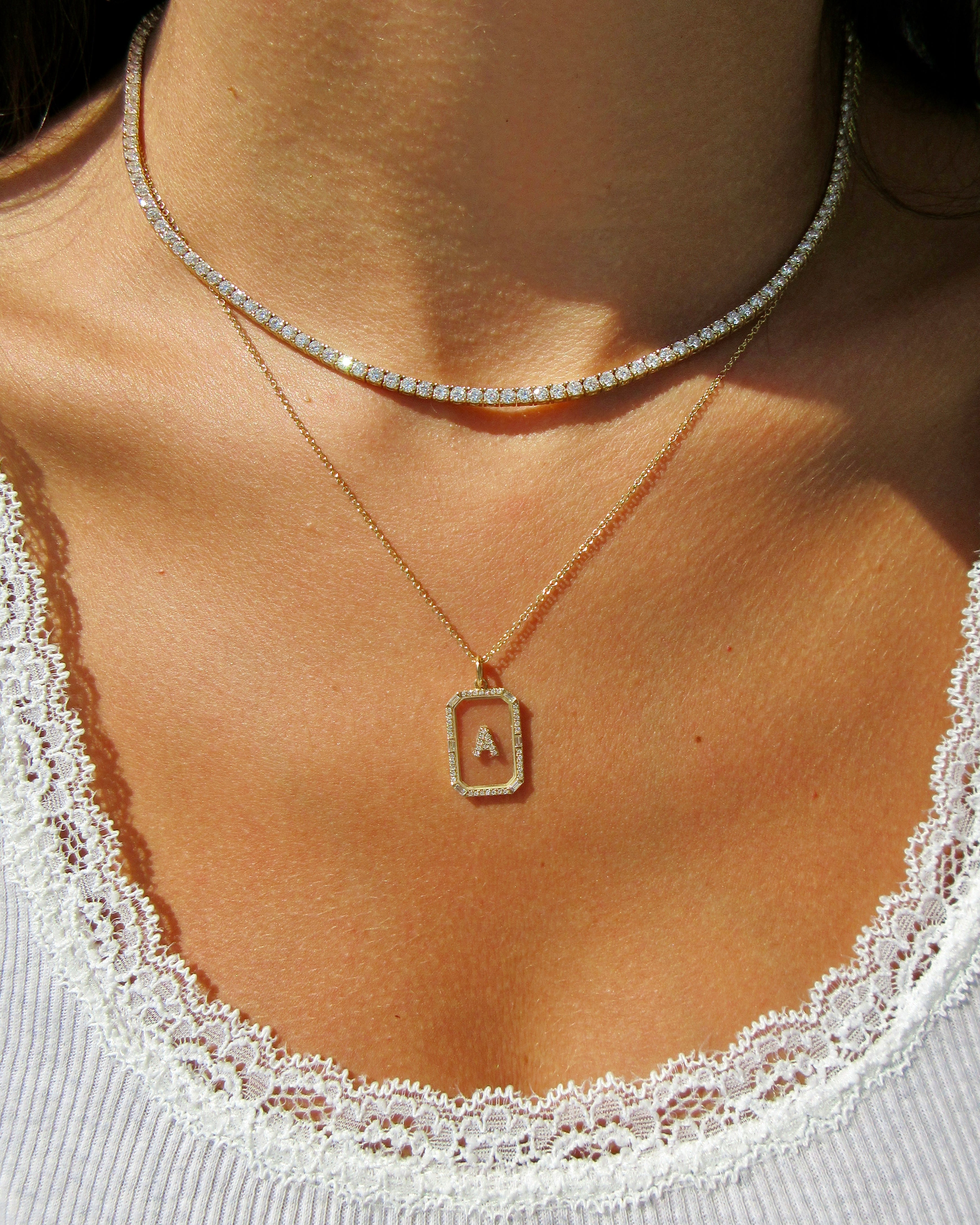 Necklace with a square pendant featuring a letter 'A' on a person wearing a white lace garment.