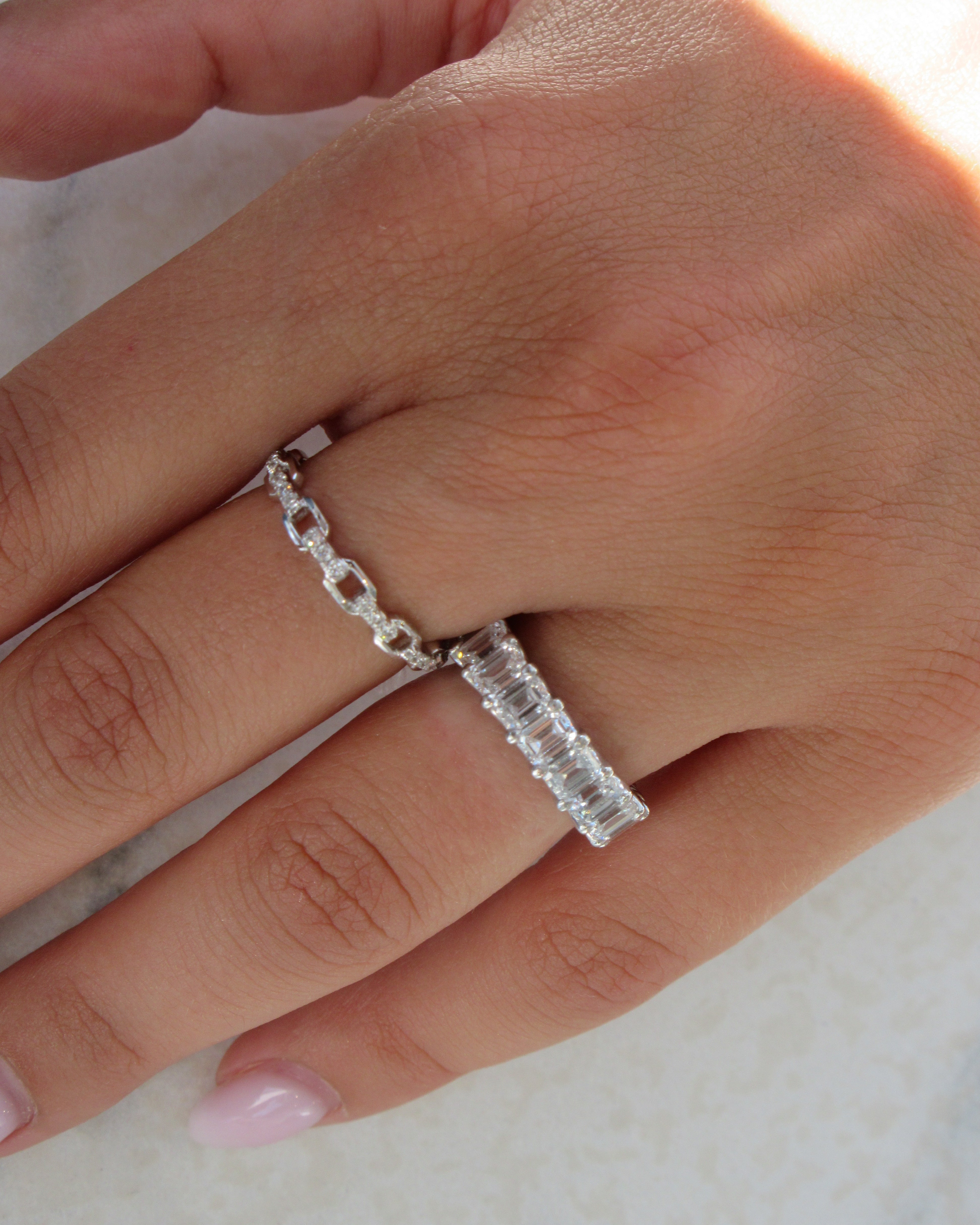 Silver ring with a diamond on a person's finger against a neutral background