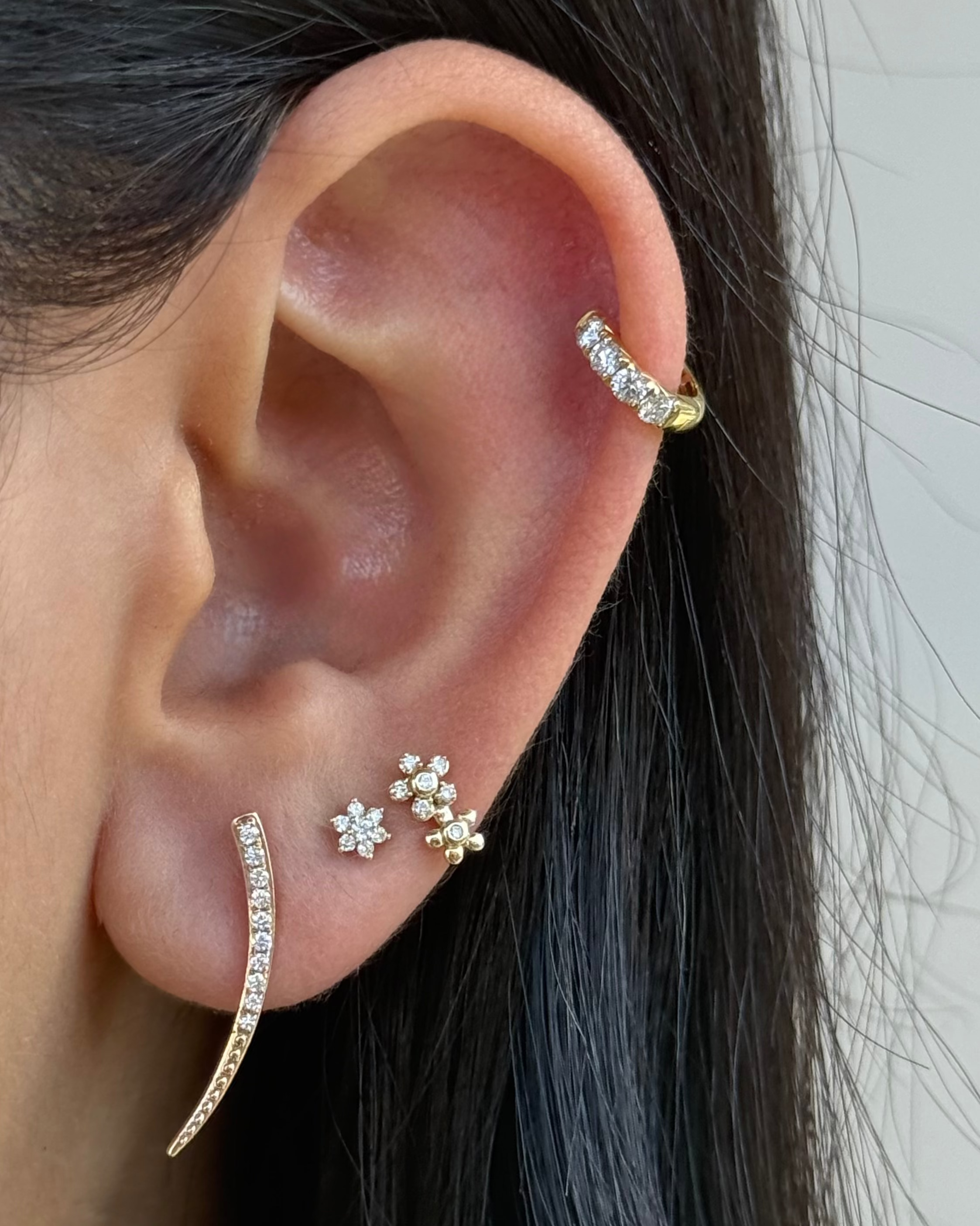 Close-up of an ear with gold and diamond earrings against a neutral background